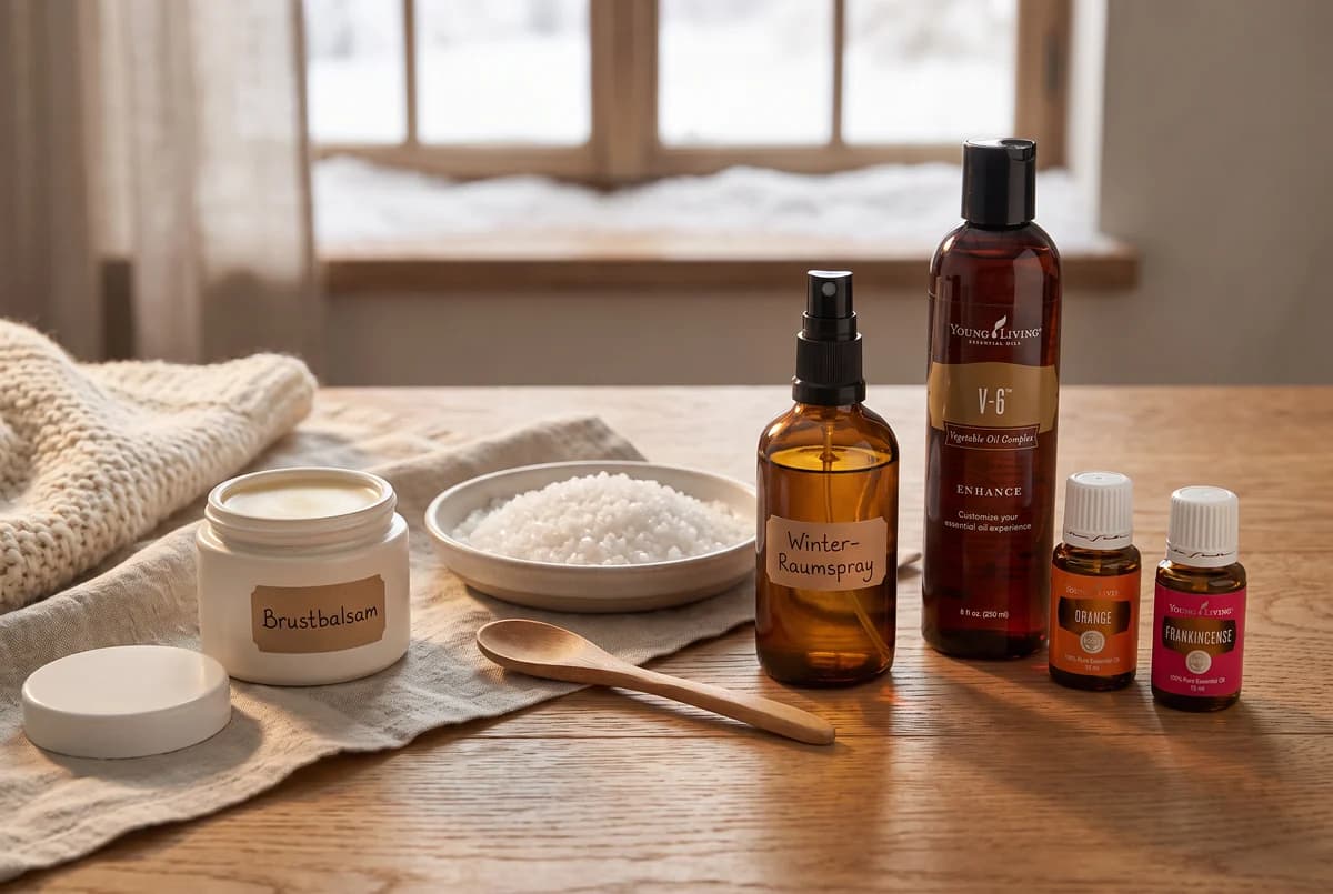 Wintertisch mit Brustbalsam, Raumspray, Trägeröl und zwei ätherischen Ölen vor einem verschneiten Fenster