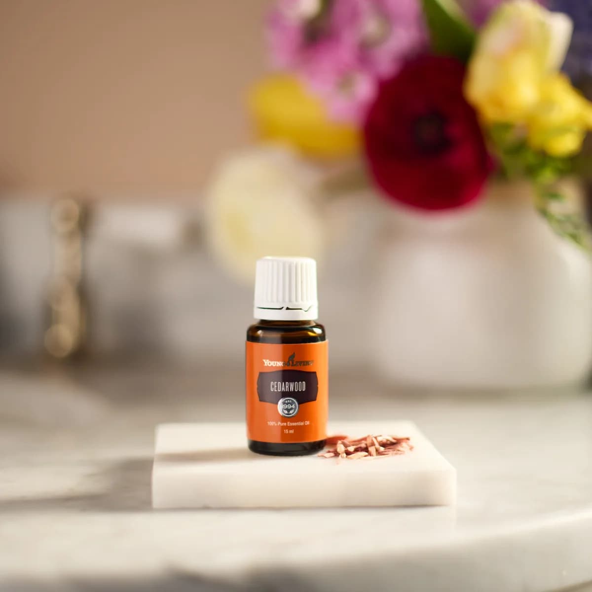 Ein Fläschchen Young Living Zedernöl 15 ml steht auf einer kleinen Marmorplatte neben rötlichen Holzspänen vor unscharfem hellem Hintergrund.