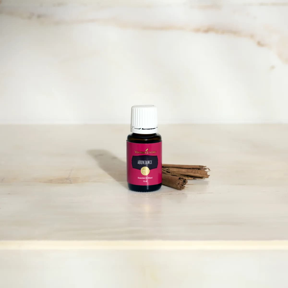 Ein Fläschchen Young Living Abundance 15 ml steht auf einer hellen Marmorfläche neben zwei Zimtstangen vor einer marmorierten Wand.