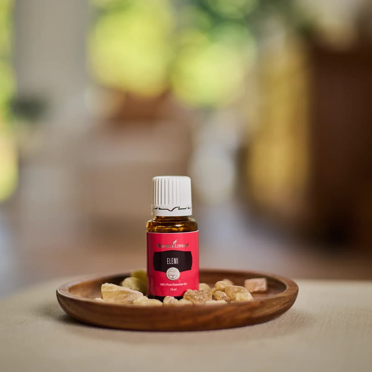 Ein Fläschchen Young Living Elemi Öl 15 ml steht in einer Holzschale mit Harzstücken auf einem hellen Tisch in einem Wohnraum.