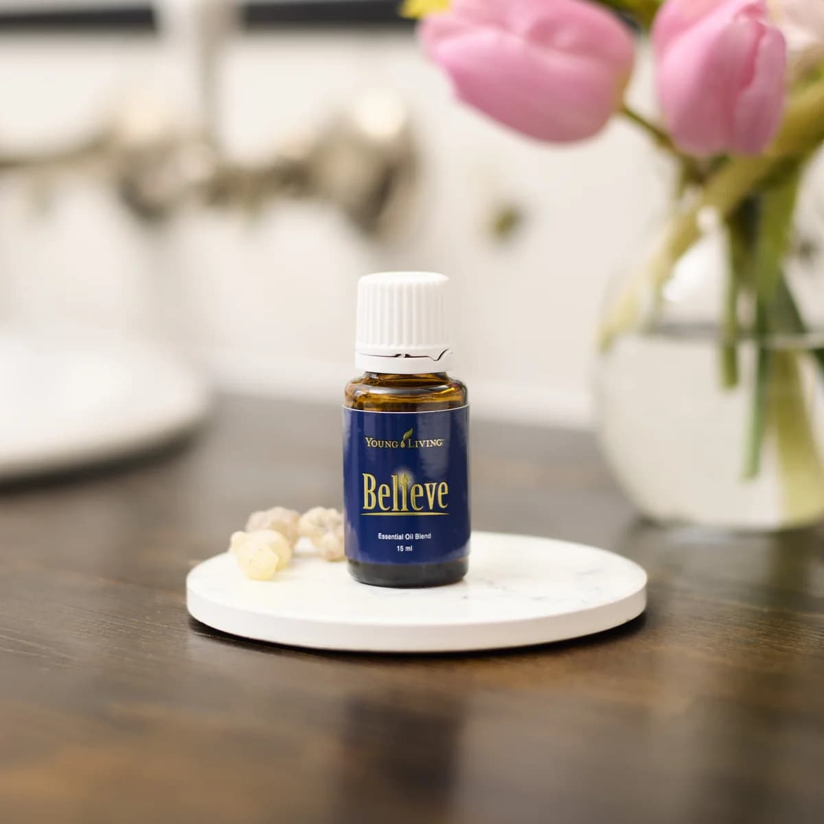 Ein Fläschchen Young Living Believe 15 ml steht auf einem weißen Marmoruntersetzer neben Harzstücken, dahinter eine Glasvase.