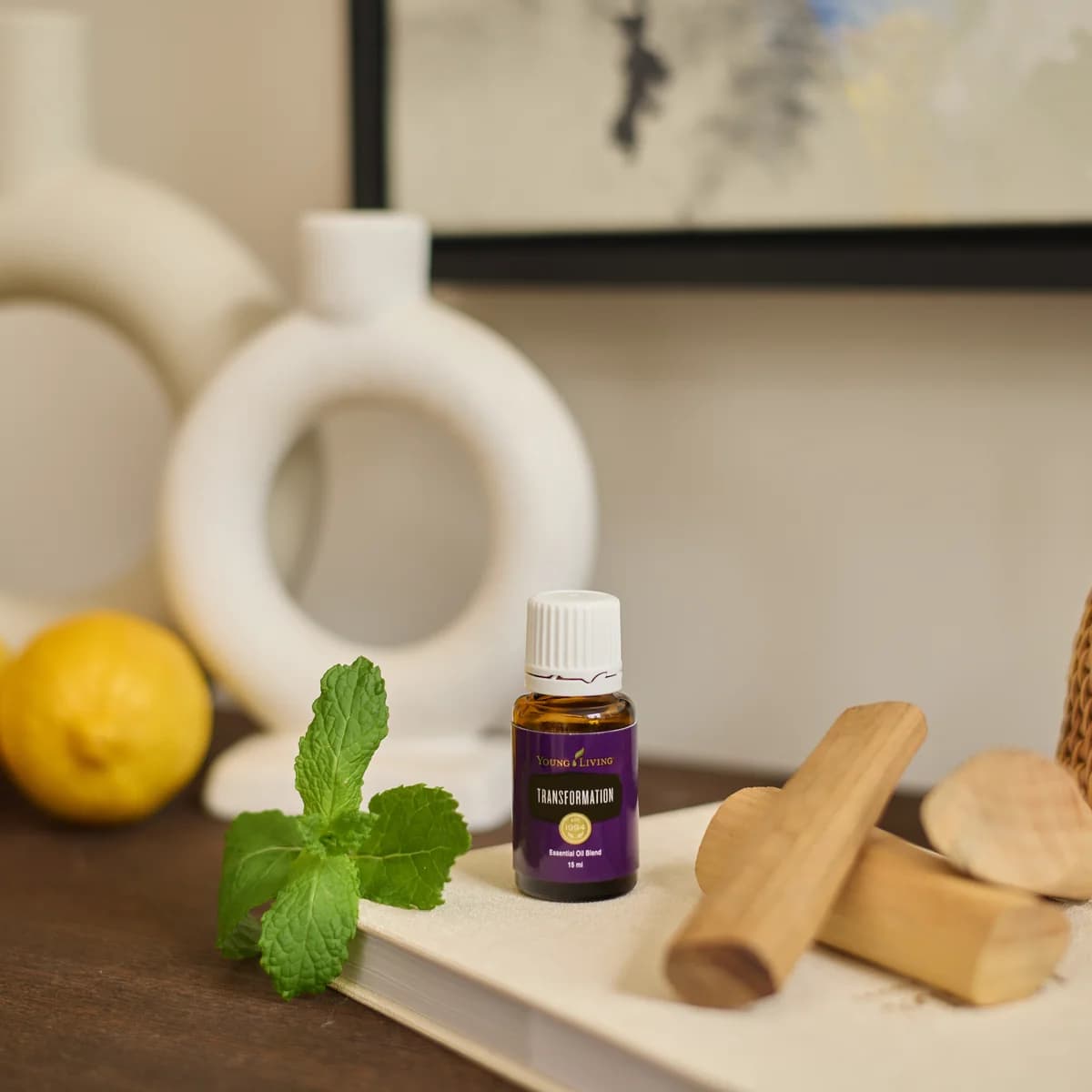 Ein Fläschchen Young Living Transformation 15 ml steht auf einem hellen Notizbuch zwischen einem Minzzweig und Holzstücken.