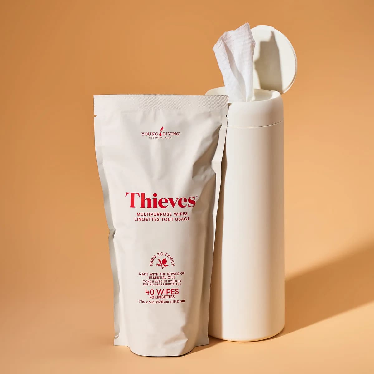 Ein Nachfüllbeutel Young Living Thieves® Multipurpose Wipes steht neben einem weißen Spender mit herausgezogenem Tuch vor orangem Hintergrund.