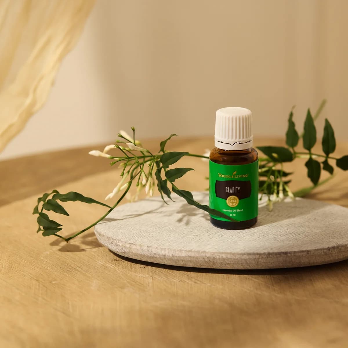 Ein Fläschchen Young Living Clarity 15 ml steht auf einer grauen Steinplatte zwischen Jasminzweigen mit weißen Blüten auf einem Holztisch.