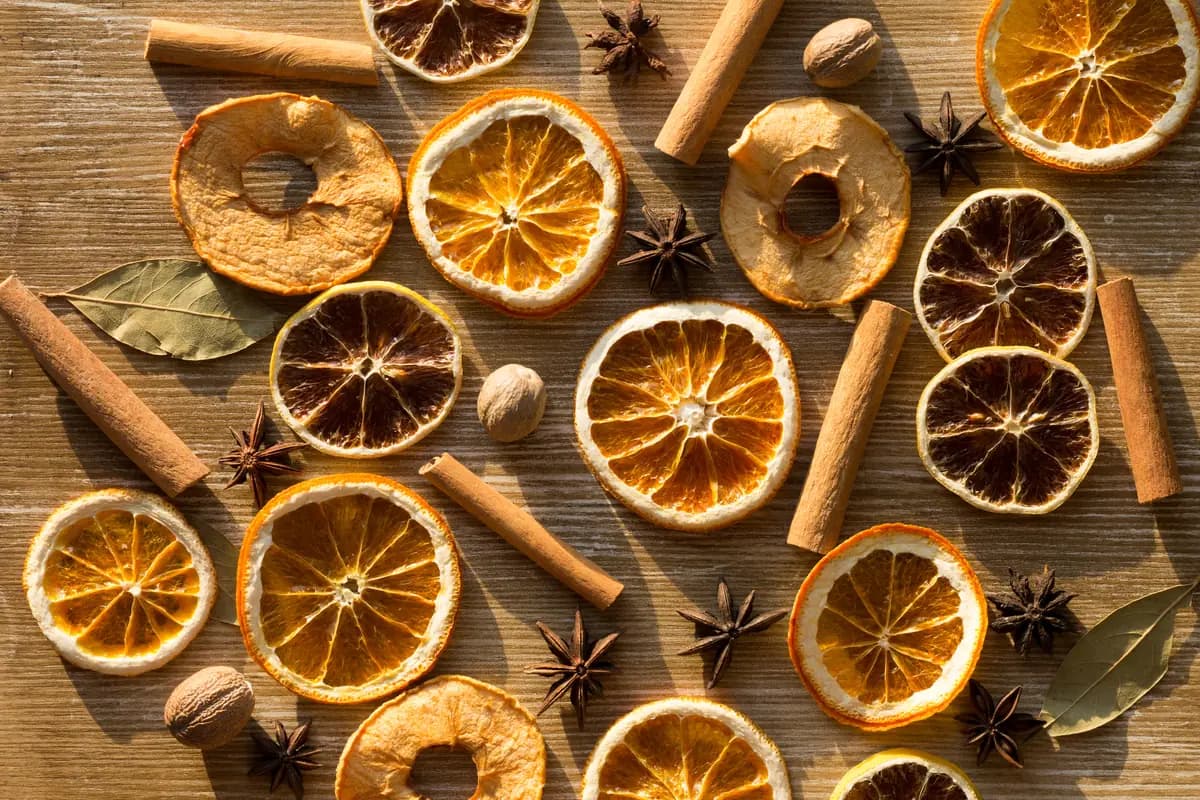 Getrocknete Orangen- und Zitronenscheiben, Zimtstangen, Sternanis und weitere Gewürze dicht beieinander im warmen Licht