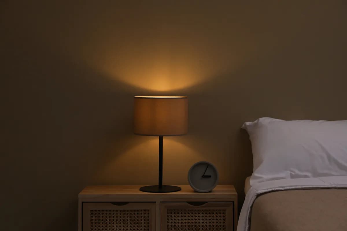 Eine warm leuchtende Nachttischlampe neben einem Bett in einem abgedunkelten Schlafzimmer