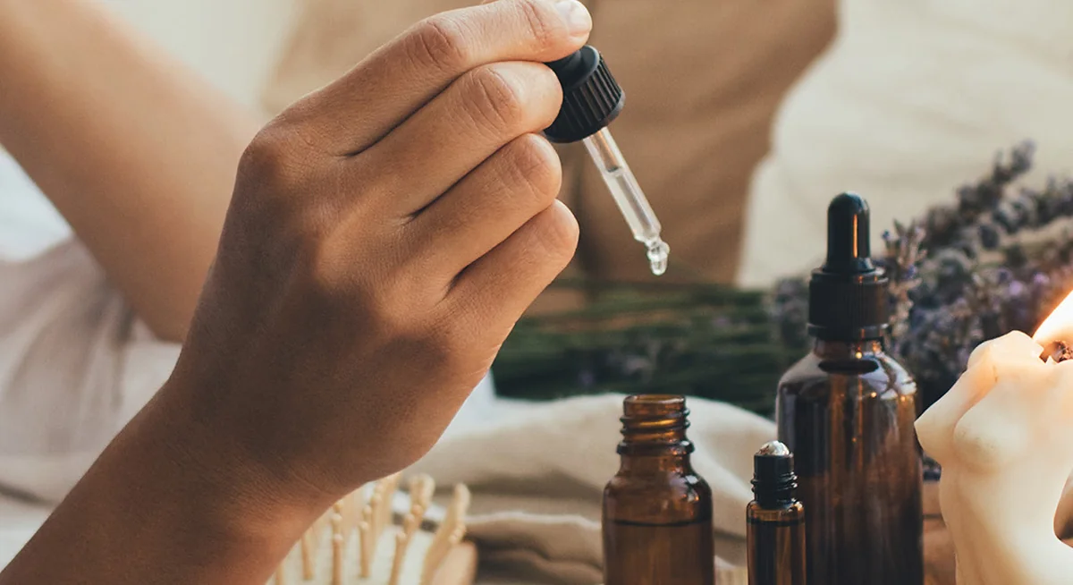 Ätherische Öle mit Pipette neben Lavendel und Kerze