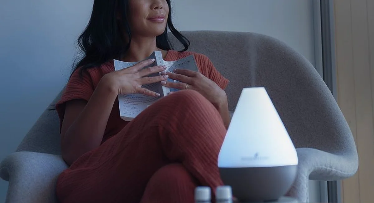 Frau entspannt im Sessel mit Buch und Diffuser