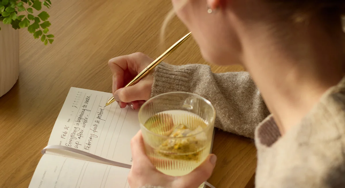 Frau schreibt in ihr Journal bei einer Tasse Tee